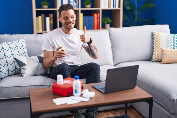 Молодий іспаномовний чоловік дивиться відео на ноутбук про те, як використовувати аптечку першої допомоги, усміхаючись щасливий і позитивний, великий палець робить відмінний знак схвалення
  - Фото, зображення