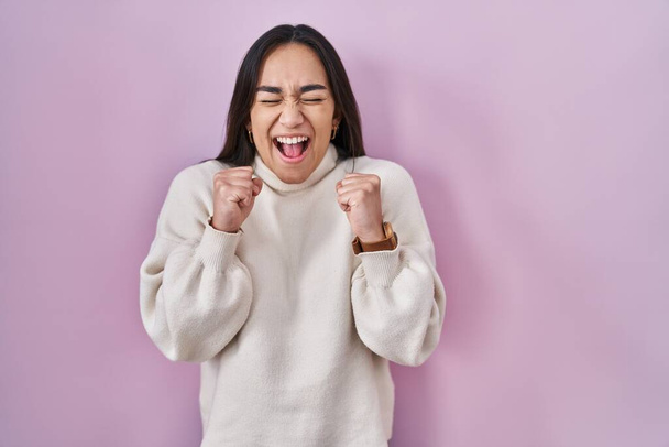 Young south asian woman standing over pink background excited for success with arms raised and eyes closed celebrating victory smiling. winner concept.  - Fotoğraf, Görsel