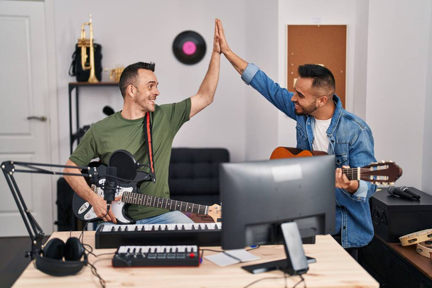 Dois músicos homens sorrindo confiante alta cinco com as mãos levantadas no estúdio de música - Foto, Imagem