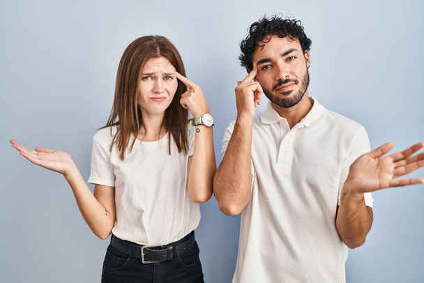 Young couple wearing casual clothes standing together confused and annoyed with open palm showing copy space and pointing finger to forehead. think about it.  - Photo, Image