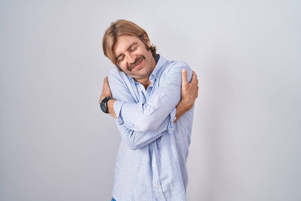 Homme caucasien avec moustache debout sur fond blanc s'étreignant heureux et positif, souriant confiant. amour de soi et soins de soi  - Photo, image