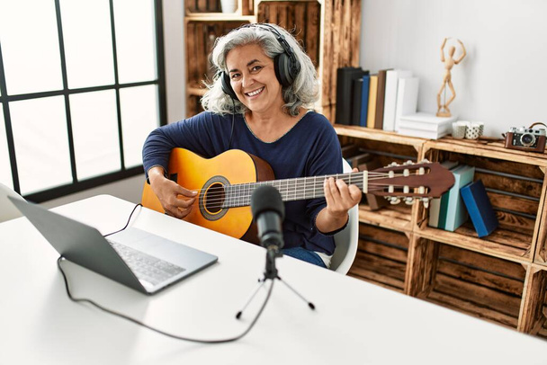 Μεσήλικη γκριζομάλλα γυναίκα που παίζει κιθάρα στο ραδιοφωνικό στούντιο. - Φωτογραφία, εικόνα