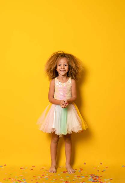 little young child girl with curly hair making party isolated over yellow background. - Foto, imagen