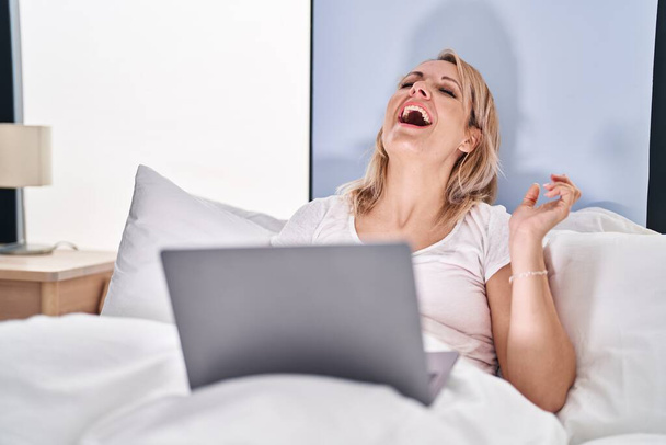 Young blonde woman having video call sitting on bed at bedroom - Zdjęcie, obraz