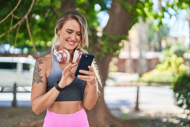 Mladá blondýna žena na sobě sportovní oblečení pomocí smartphone v parku - Fotografie, Obrázek