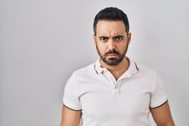Young hispanic man with beard wearing casual clothes over white background skeptic and nervous, frowning upset because of problem. negative person.  - Photo, Image