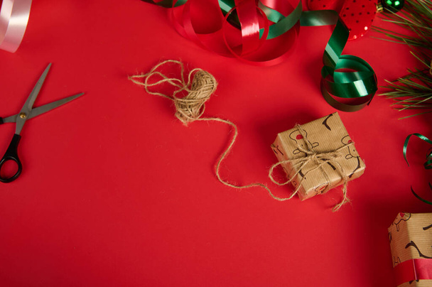 Weihnachts- oder Neujahrsgeschenke, eingewickelt in ein Geschenkpapier mit Hirschmuster und mit Leinenband gebunden, ausgelegt mit grünem, glänzendem Band, isoliert über rotem Hintergrund mit Kopierplatz. Geschenke verpacken. - Foto, Bild