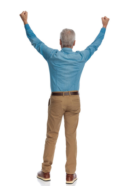 back view of old man with grey hair holding fists above head and celebrating victory on white background - Фото, зображення