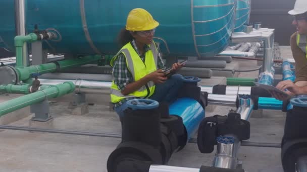 Young woman and man engineer examining pipeline and looking digital tablet in the factory, mechanic or technician inspector plumber valve and talking together, industrial and maintenance concept. - Felvétel, videó