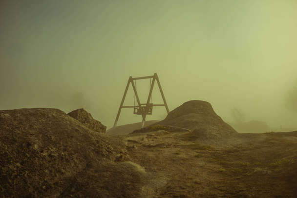Гойдалка в місці з еродованими каменями і туманом, який приховує сонце
 - Фото, зображення