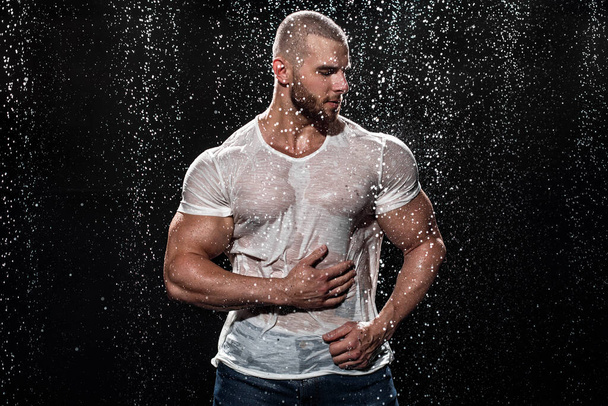 Muscular man under the rain in studio. Sexy male in water drops - Фото, изображение