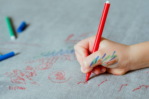 Dítě je potřísněné inkoustem a na čalounění pohovky kreslí červenou značkou. Nábytkovou látku. Čistící koncept. Kvalitní fotografie - Fotografie, Obrázek