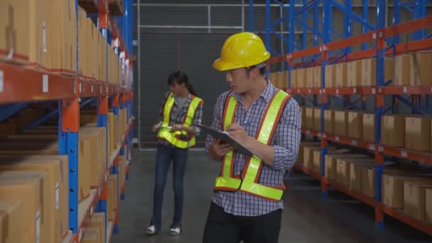Young man and woman worker check stock and inspection with document on clipboard in the warehouse at factory, worker working at storehouse, logistic and cargo, shipping and distribution. - Video