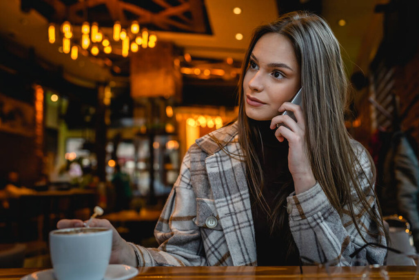 One woman young adult caucasian female sit at cafe alone using mobile phone talk copy space - Valokuva, kuva