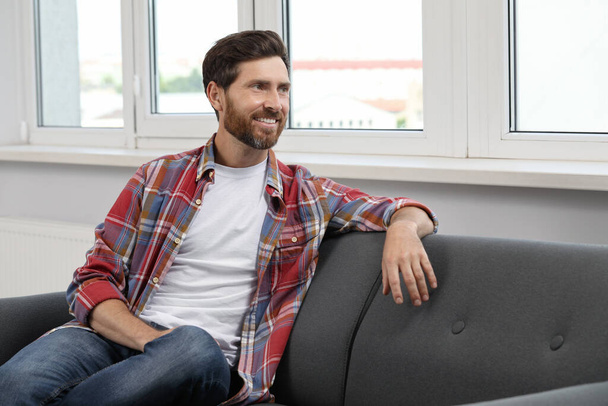 Smiling bearded man looking away on sofa indoors - Фото, зображення