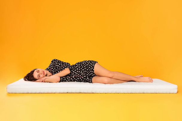 Young woman sleeping on soft mattress against orange background - Zdjęcie, obraz