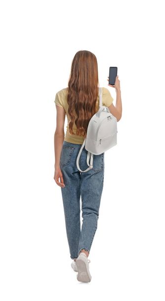 Young woman in casual outfit using smartphone while walking on white background, back view - Fotó, kép