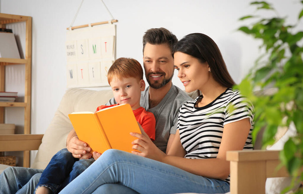 Happy family reading book together on sofa in living room at home - Фото, изображение