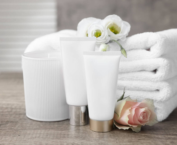 Cosmetic products, scented candle and folded towels with flowers on wooden table indoors - Fotó, kép