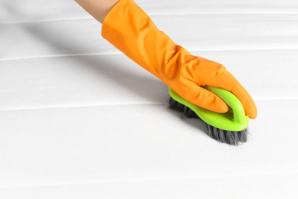 Woman in orange gloves cleaning white mattress with brush, closeup. Space for text - Foto, afbeelding