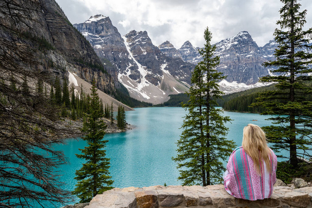 ピンクの毛布に身を包んだブロンドの女性のバックビュー、カナダのモラニー湖を見て - 写真・画像