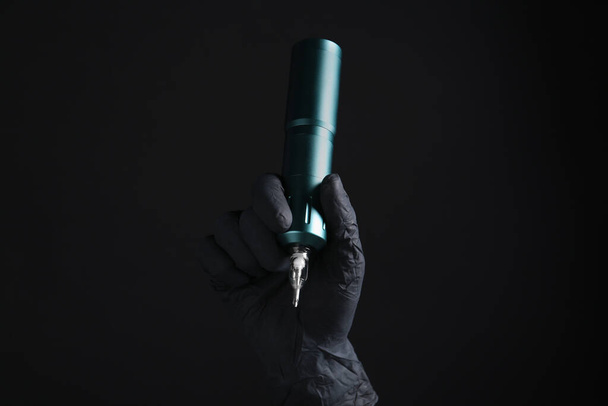 Professional tattoo artist with machine on black background, closeup - Fotoğraf, Görsel