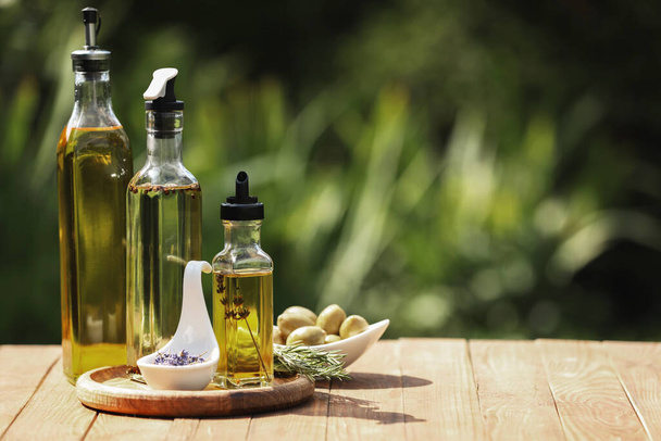 Different cooking oils and ingredients on wooden table against blurred green background, space for text - 写真・画像