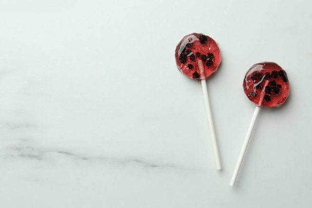 Sweet colorful lollipops with berries on white marble table, flat lay. Space for text - 写真・画像