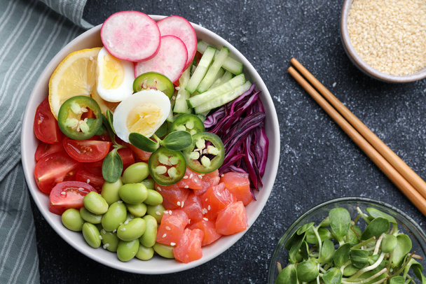 Poke bowl with salmon, edamame beans and vegetables on black table, flat lay - Fotoğraf, Görsel