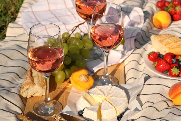 Glasses of delicious rose wine and food on white picnic blanket outdoors - Foto, Bild