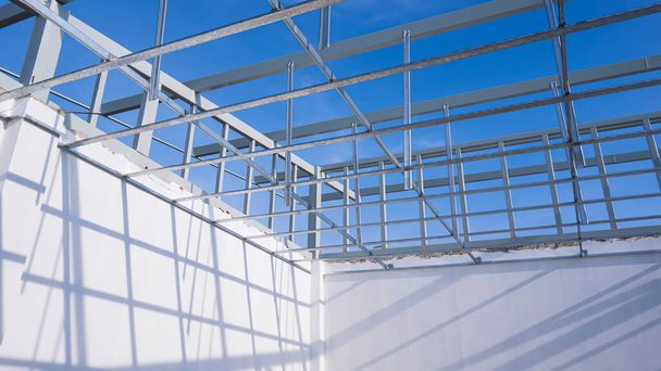 Aluminium c-line plafondstructuur met witte betonnen wand in huis bouwplaats tegen blauwe lucht achtergrond, lage hoek en perspectief uitzicht - Foto, afbeelding