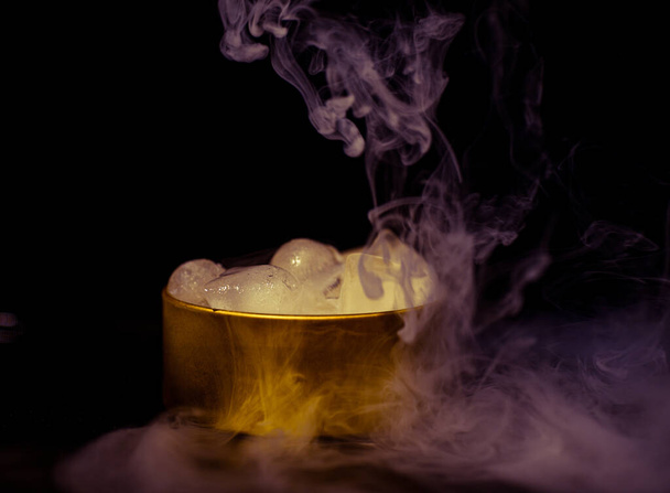 Glace dans une boîte dorée avec fumée, fumée colorée, fumée bleue, fumée grise, glace au sirop, glace délicieuse. image de l'espace sur fond sombre - Photo, image