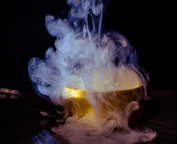 Πάγος σε χρυσό κουτί με καπνό, πολύχρωμο καπνό, μπλε καπνό, γκρι καπνό, πάγος σε σιρόπι, νόστιμο πάγο. διαστημική εικόνα σε σκούρο φόντο - Φωτογραφία, εικόνα