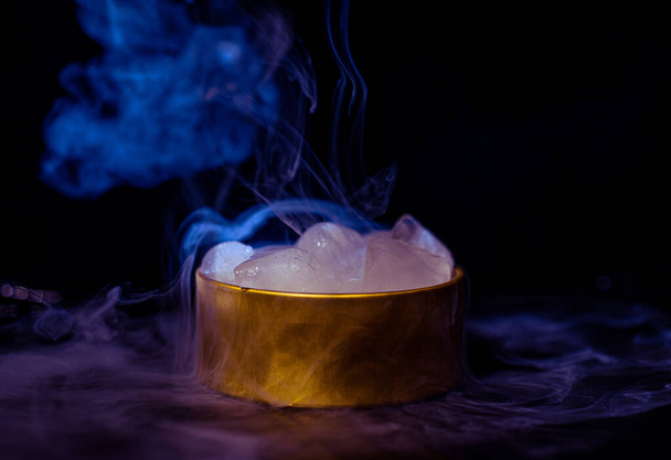 Eis in einer goldenen Schachtel mit Rauch, buntem Rauch, blauem Rauch, grauem Rauch, Eis in Sirup, köstlichem Eis. Raumbild auf dunklem Hintergrund - Foto, Bild