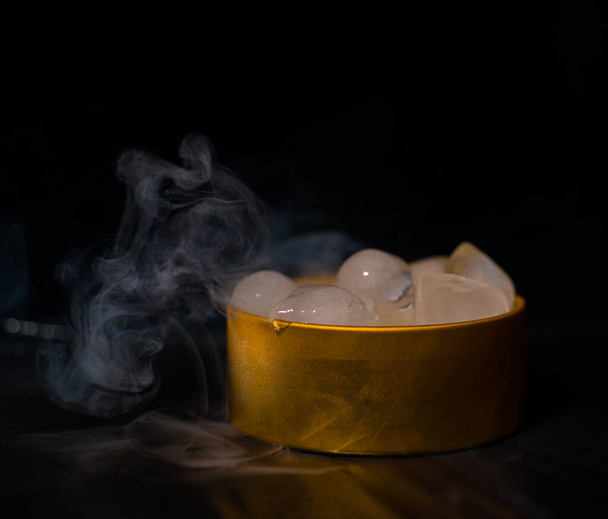 Glace dans une boîte dorée avec fumée, fumée colorée, fumée bleue, fumée grise, glace au sirop, glace délicieuse. image de l'espace sur fond sombre - Photo, image