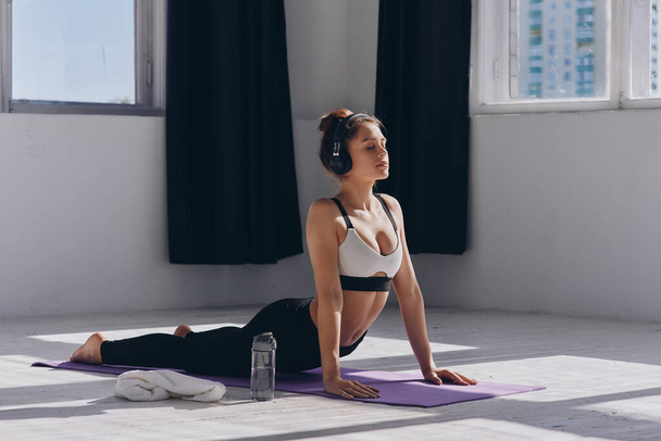 Confident young woman in headphones keeping eyes closed while practicing yoga in studio - Foto, Bild
