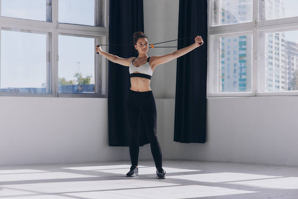 Confident young woman exercising with resistance band while standing in front of the window - Foto, Imagem