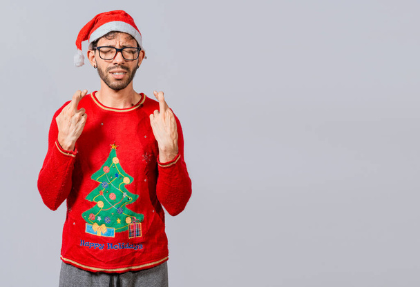 Kerl mit Weihnachtsmütze macht einen Wunsch auf isoliertem Hintergrund, Hoffnungsvoller Mann in Weihnachtskleidung macht einen Wunsch, schöner Mann mit Weihnachtsmütze macht einen Wunsch auf weißem Hintergrund - Foto, Bild