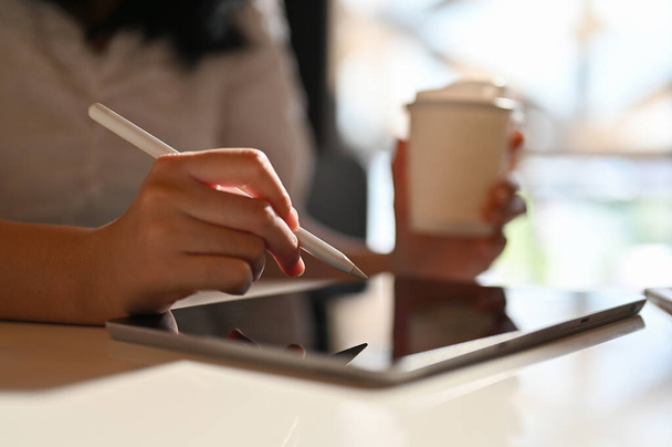 Asiatische Freiberuflerin mit ihrem digitalen Tablet und Stift, Fernarbeit im Coffeeshop-Co-Working-Space. Seitenansicht, abgeschnittener Schuss - Foto, Bild