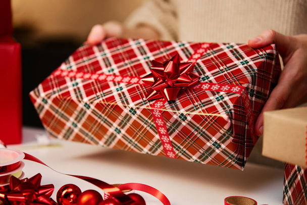 Sıcak süveter giymiş bir kadın hediye kutusunu hediye kağıdına sarmış, şenlikli kurdeleyle. Kış tatili hediyesi. Noel ve Mutlu Yıllar Kutlaması - Fotoğraf, Görsel