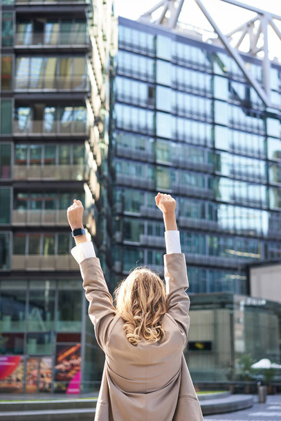 Вид ззаду на корпоративну жінку, юрист, який святкує, піднімає руки і тріумфує, досягає мети або успіху, стоїть на вулиці центру міста
. - Фото, зображення