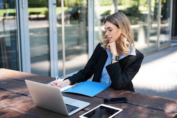 Udana bizneswoman pracująca na świeżym powietrzu. Corporate kobieta siedzi na ławce z laptopem, pisanie, notatki podczas spotkania w pracy. - Zdjęcie, obraz