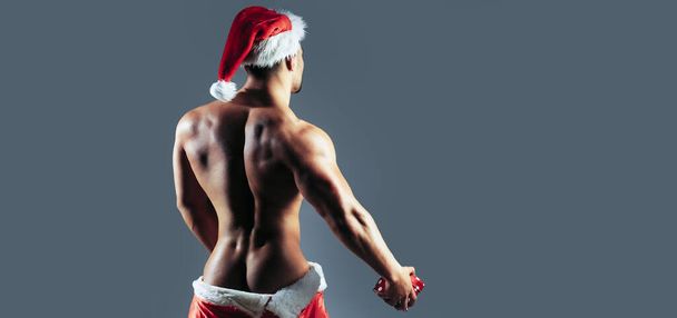 Back of men gay in santa hat. New year strip and gifts for adults. Muscle gay at xmas. Santa gay with muscular body. Christmas party and sex games. Handsome sexy santa fo gay club banner - Fotografie, Obrázek