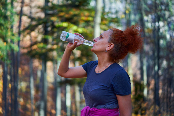Woman hiker drinking water after a steep trail climb in the forest mountains - Fotografie, Obrázek