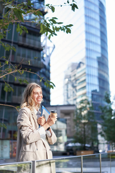 Belle femme d'affaires se sent excitée, boissons café à emporter près du centre d'affaires à l'extérieur, se tient sur la rue de la ville et sourit. - Photo, image