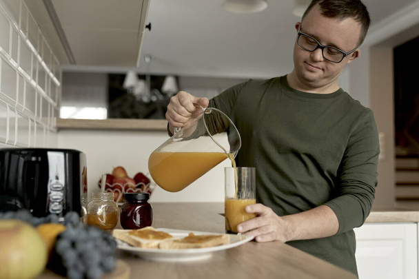 Volwassen blanke man met donssyndroom bereidt ontbijt voor - Foto, afbeelding