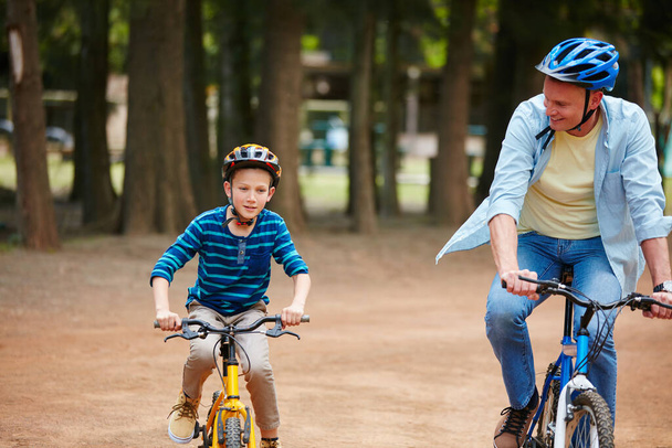 Pärjäät hienosti, poika. isä ja hänen nuori poikansa ajavat polkupyörillä puistossa - Valokuva, kuva