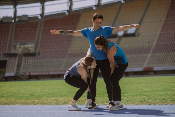 Beautiful sports girls are about to lift their male friend up. They are having fun at the stadium - Φωτογραφία, εικόνα