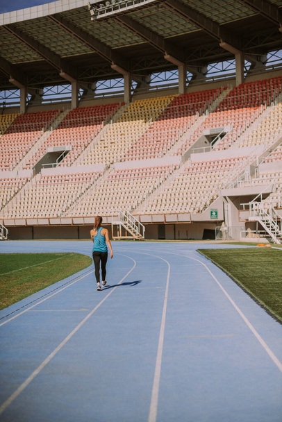 Ένα κορίτσι περπατάει στο γήπεδο σε μια αθλητική πίστα μετά το τζόκινγκ. - Φωτογραφία, εικόνα