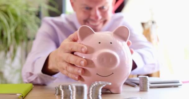 Smiling emotionally happy businessman strokes piggy bank. Profitable financial cash investment and business budget - Footage, Video